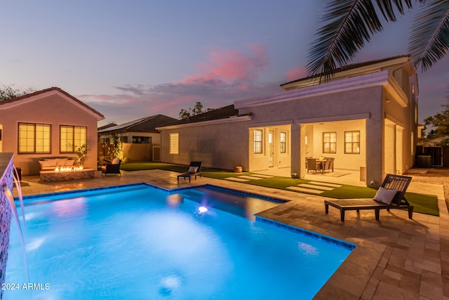 pool at dusk with pool water feature, a patio, and an outdoor fire pit