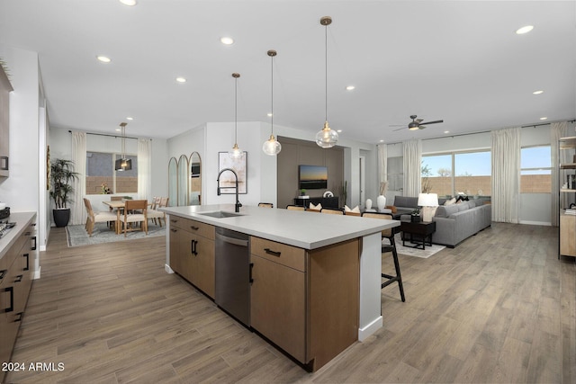 kitchen with light wood-type flooring, stainless steel dishwasher, ceiling fan, sink, and an island with sink