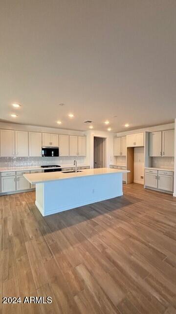 kitchen featuring light wood-type flooring, backsplash, sink, white cabinets, and an island with sink