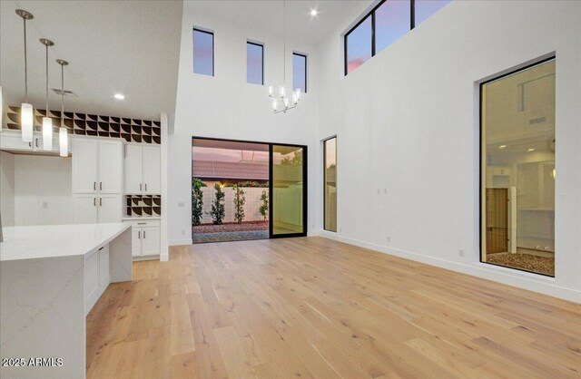 unfurnished living room with a towering ceiling, a chandelier, and light wood-type flooring