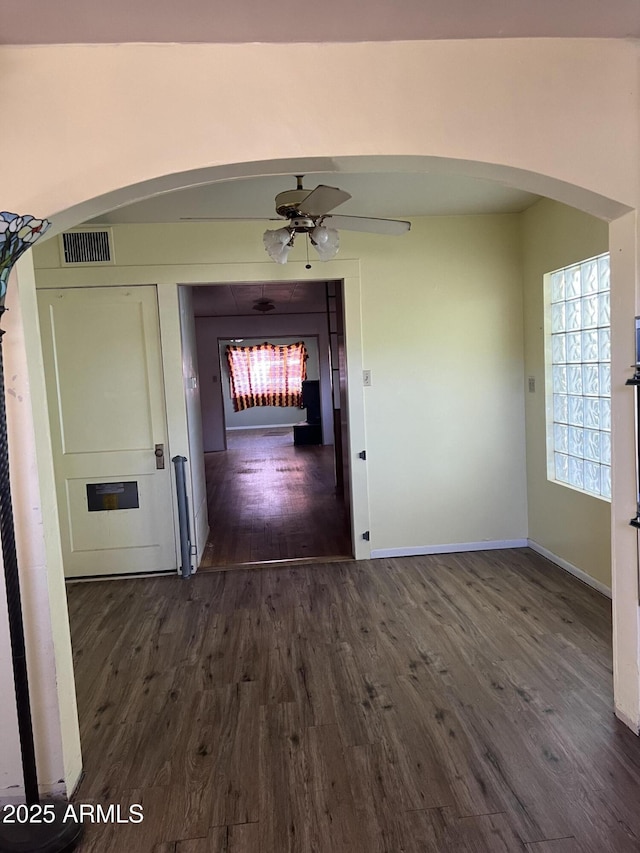 hallway featuring arched walkways, baseboards, dark wood finished floors, and visible vents