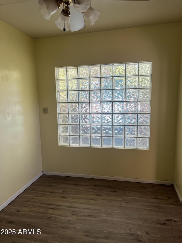 spare room featuring baseboards, ceiling fan, a wealth of natural light, and dark wood-type flooring