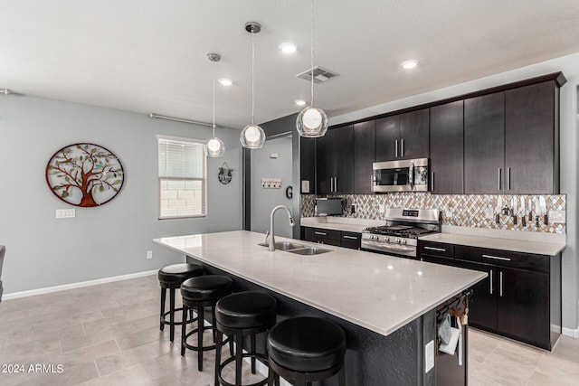 kitchen with an island with sink, sink, decorative light fixtures, backsplash, and appliances with stainless steel finishes