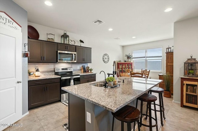 kitchen featuring an island with sink, appliances with stainless steel finishes, dark brown cabinets, and sink