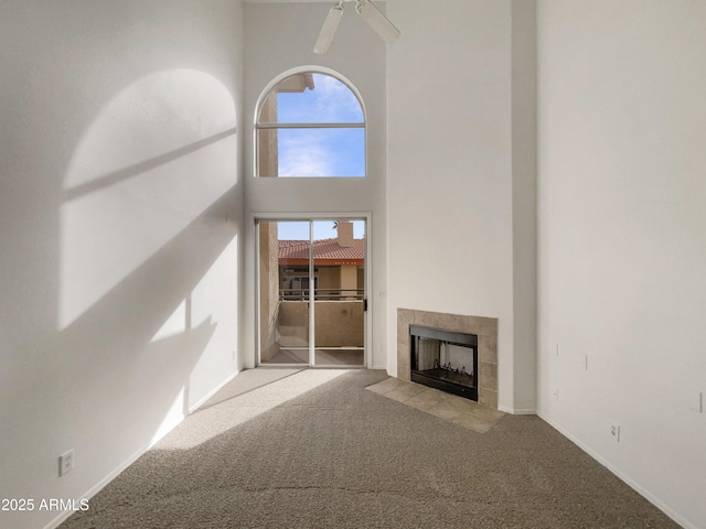 unfurnished living room with a ceiling fan, carpet flooring, a towering ceiling, and a tiled fireplace