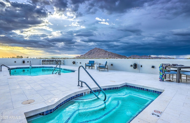 pool at dusk featuring a mountain view and a patio