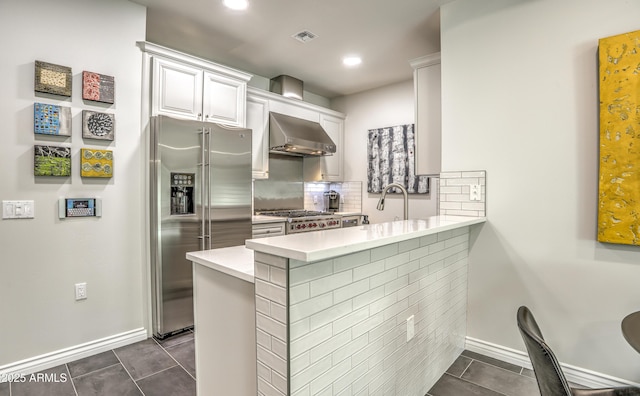 kitchen with stainless steel refrigerator with ice dispenser, kitchen peninsula, white cabinets, and wall chimney exhaust hood