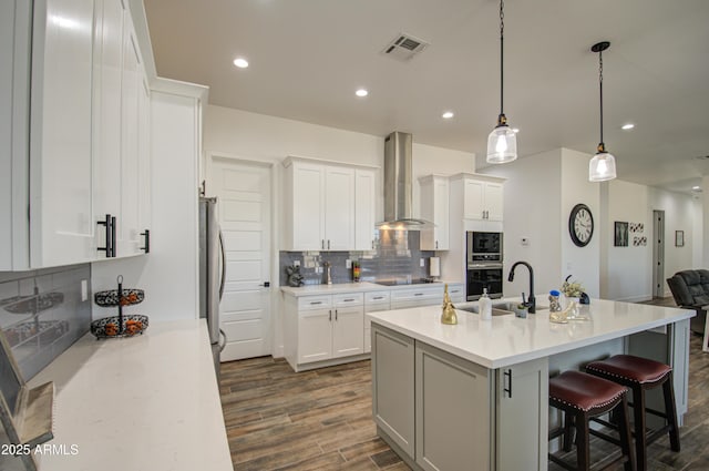 kitchen featuring wall chimney exhaust hood, sink, white cabinetry, decorative light fixtures, and appliances with stainless steel finishes