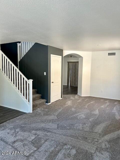 unfurnished room featuring dark carpet and a textured ceiling