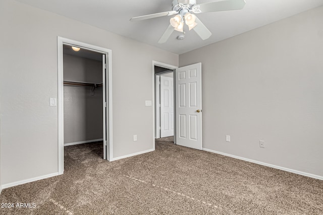 unfurnished bedroom featuring a spacious closet, dark carpet, a closet, and ceiling fan