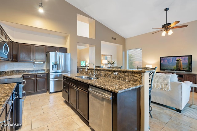 kitchen with sink, a kitchen island with sink, dark stone countertops, stainless steel appliances, and high vaulted ceiling