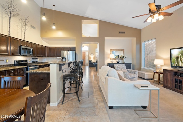 kitchen with pendant lighting, high vaulted ceiling, dark stone counters, stainless steel appliances, and dark brown cabinets