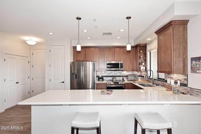 kitchen with sink, stainless steel appliances, kitchen peninsula, decorative light fixtures, and a breakfast bar area