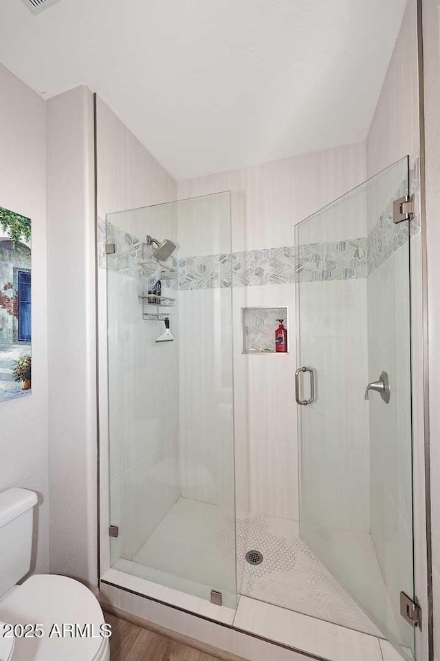 bathroom with wood-type flooring, a shower with shower door, and toilet