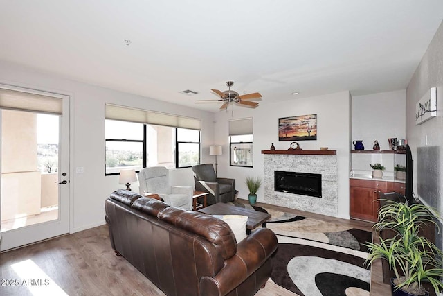 living room with a stone fireplace, ceiling fan, plenty of natural light, and light hardwood / wood-style floors