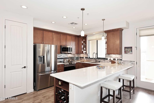 kitchen featuring sink, hanging light fixtures, stainless steel appliances, a breakfast bar, and light wood-type flooring