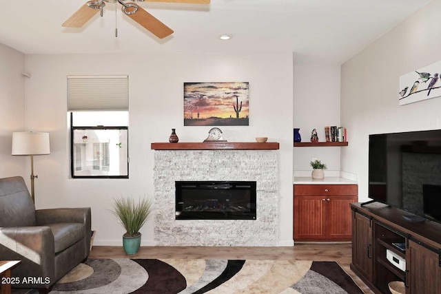 living room with ceiling fan, a stone fireplace, and light hardwood / wood-style flooring