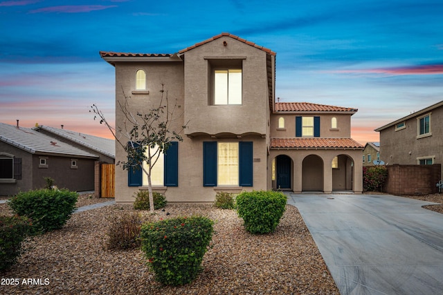 mediterranean / spanish-style home with a tiled roof, fence, and stucco siding