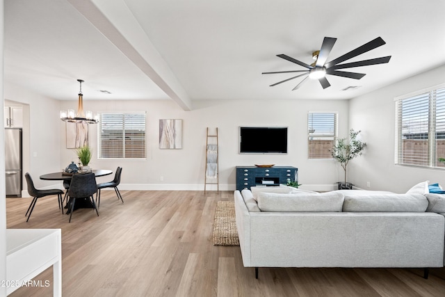 living area featuring baseboards, beamed ceiling, light wood finished floors, and ceiling fan with notable chandelier