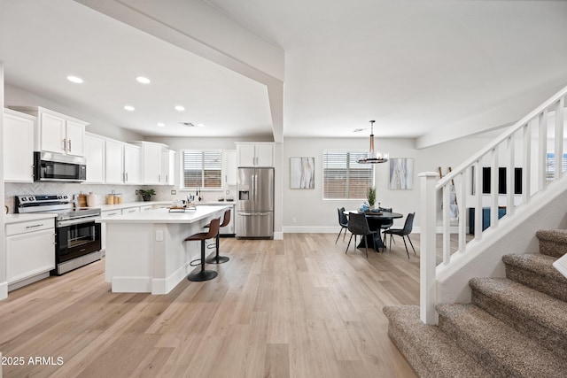 kitchen with stainless steel appliances, white cabinetry, light wood-style floors, tasteful backsplash, and a kitchen bar