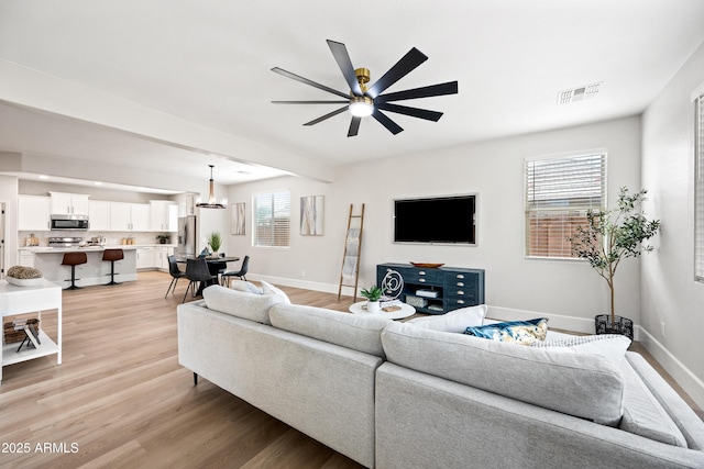 living area with light wood-style flooring, visible vents, ceiling fan, and baseboards