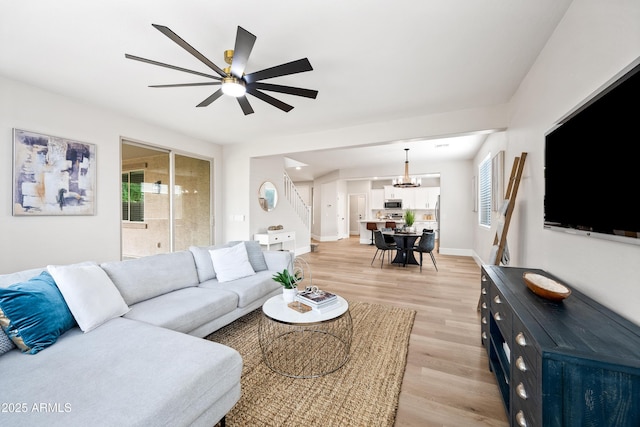 living room with stairs, ceiling fan, light wood finished floors, and baseboards