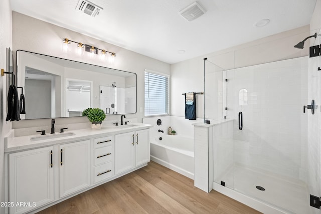 bathroom featuring a garden tub, wood finished floors, a sink, and a stall shower