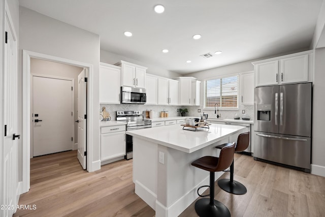 kitchen featuring visible vents, light wood-style flooring, appliances with stainless steel finishes, white cabinets, and a kitchen bar