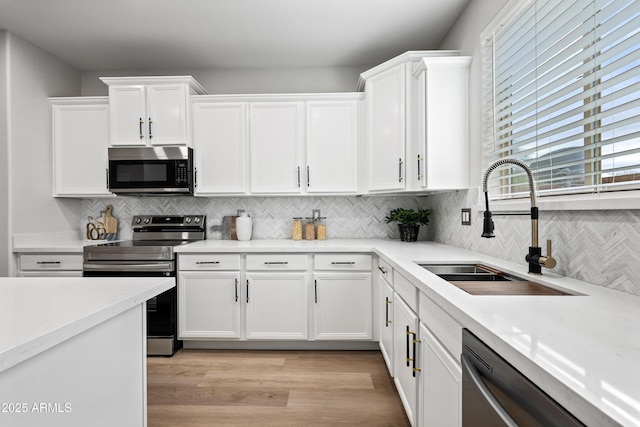 kitchen with white cabinets, appliances with stainless steel finishes, light countertops, light wood-type flooring, and a sink