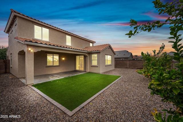 back of property at dusk featuring a tile roof, a yard, stucco siding, a patio area, and a fenced backyard