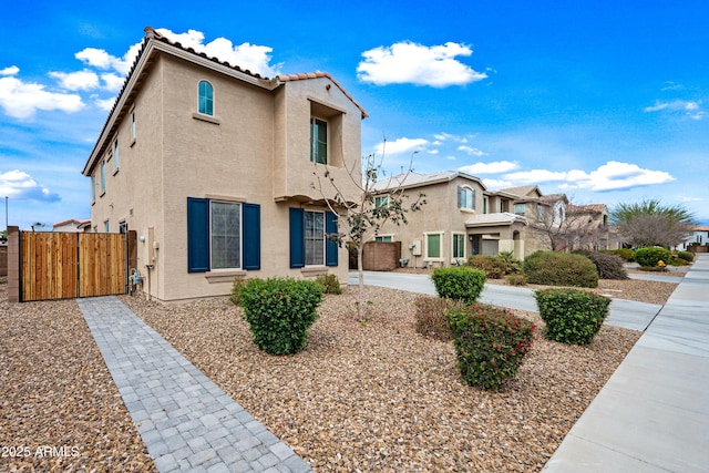 view of front of house with a tile roof, fence, a gate, and stucco siding