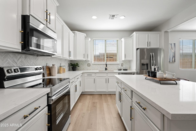 kitchen with a wealth of natural light, appliances with stainless steel finishes, a sink, and white cabinetry