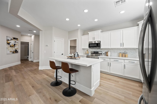 kitchen featuring visible vents, decorative backsplash, appliances with stainless steel finishes, a center island, and a kitchen bar