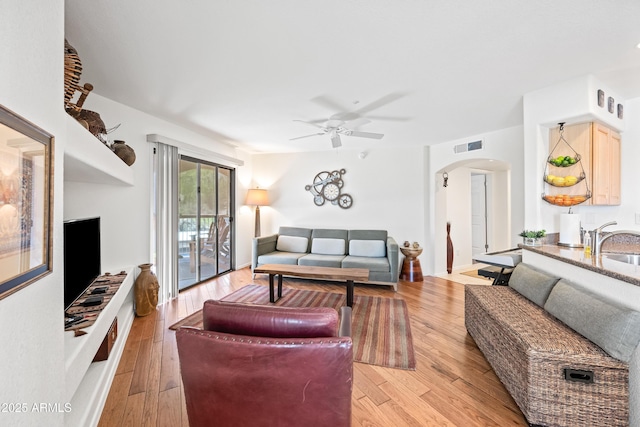 living room featuring light wood-style floors, a ceiling fan, arched walkways, and visible vents