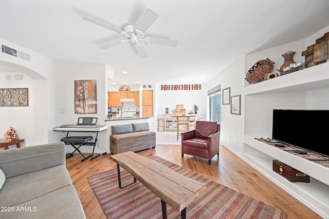 living area featuring visible vents, arched walkways, ceiling fan, and light wood-type flooring