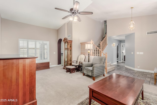 carpeted living area with a ceiling fan, visible vents, arched walkways, high vaulted ceiling, and stairs
