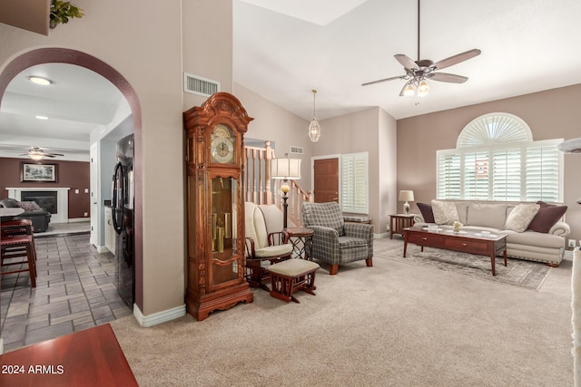 carpeted living room featuring arched walkways, a ceiling fan, baseboards, vaulted ceiling, and visible vents