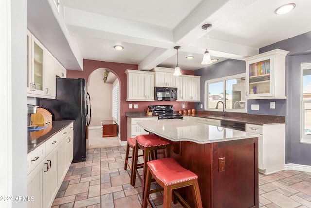 kitchen featuring baseboards, a kitchen bar, beamed ceiling, black appliances, and stone tile flooring