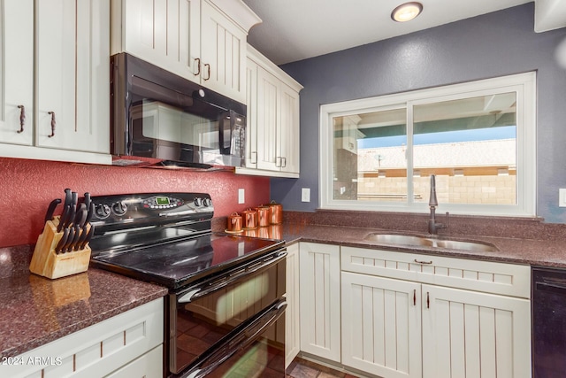 kitchen with a sink, dark stone counters, black appliances, and white cabinets