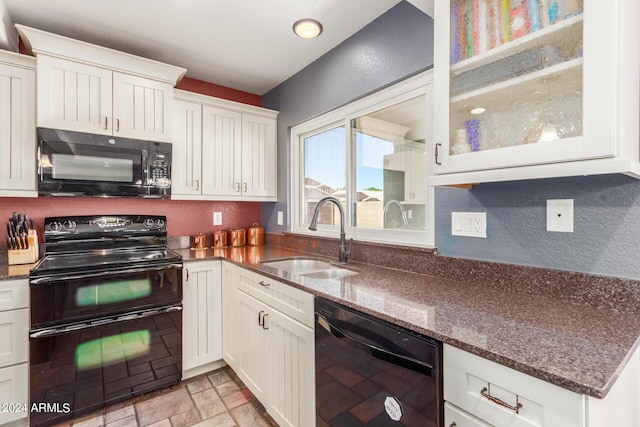 kitchen with a sink, white cabinets, black appliances, glass insert cabinets, and dark stone counters
