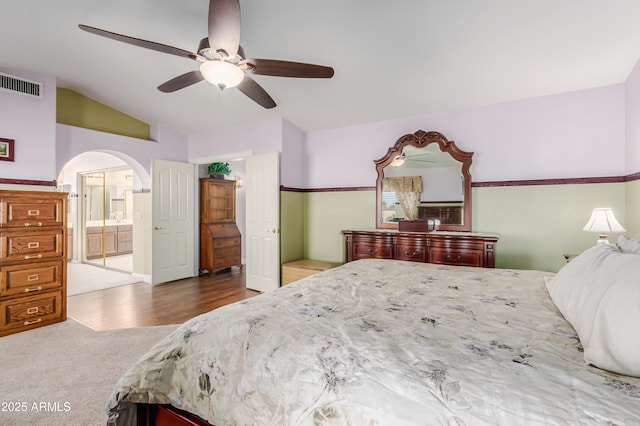 carpeted bedroom featuring visible vents, ceiling fan, connected bathroom, arched walkways, and vaulted ceiling
