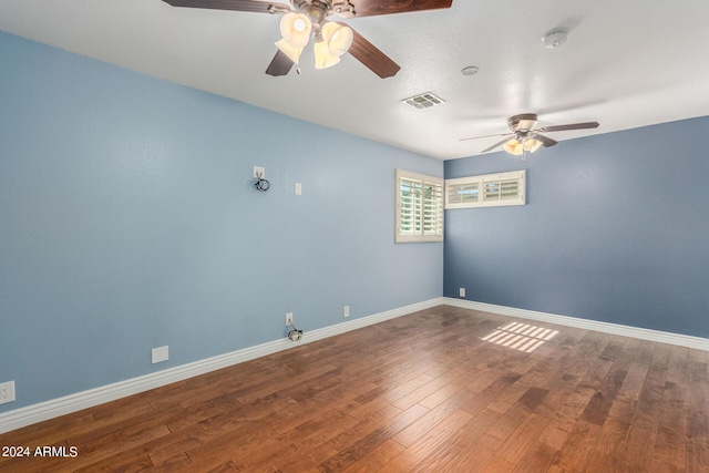 empty room featuring a ceiling fan, baseboards, visible vents, and wood finished floors