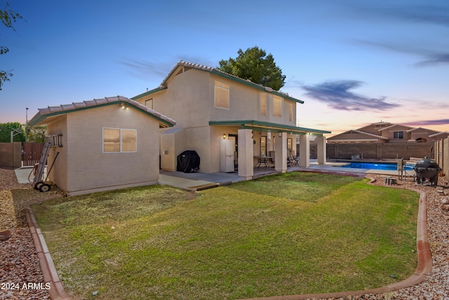 back of property at dusk with a fenced backyard, a fenced in pool, stucco siding, and a yard