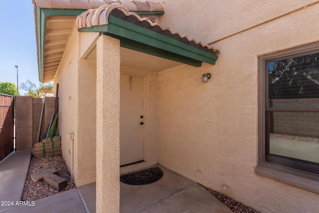 entrance to property with stucco siding, a tile roof, and fence