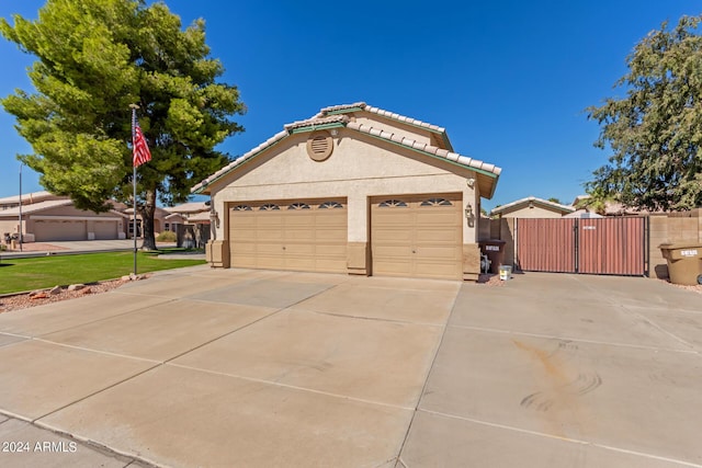 view of front of house featuring a tiled roof, a gate, concrete driveway, an attached garage, and stucco siding