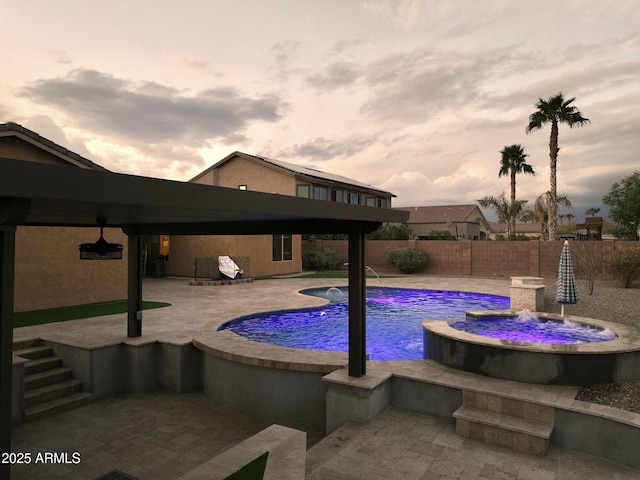 pool at dusk featuring pool water feature, a jacuzzi, and a patio