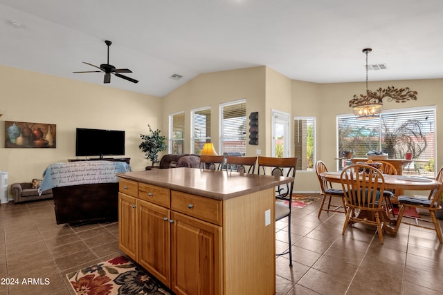 kitchen featuring a kitchen breakfast bar, vaulted ceiling, ceiling fan with notable chandelier, a kitchen island, and decorative light fixtures