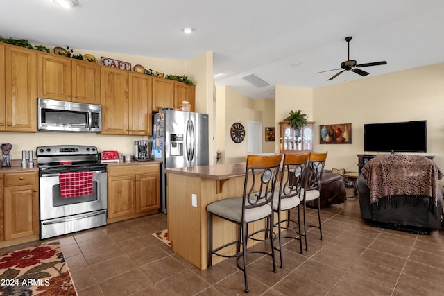 kitchen with appliances with stainless steel finishes, a center island, ceiling fan, and dark tile patterned flooring