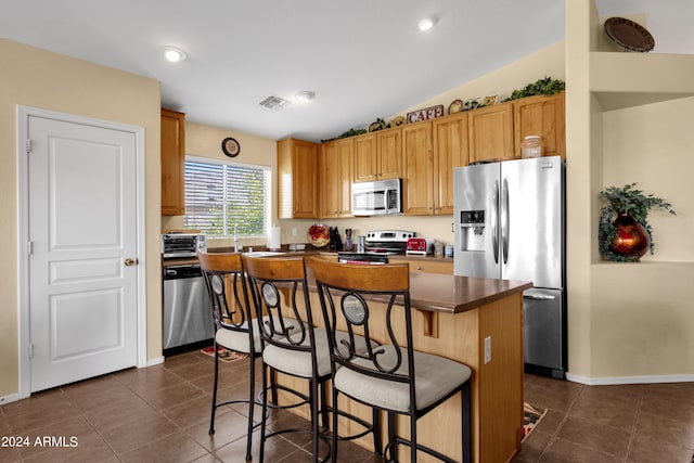 kitchen featuring a breakfast bar, dark tile patterned flooring, a center island, vaulted ceiling, and stainless steel appliances