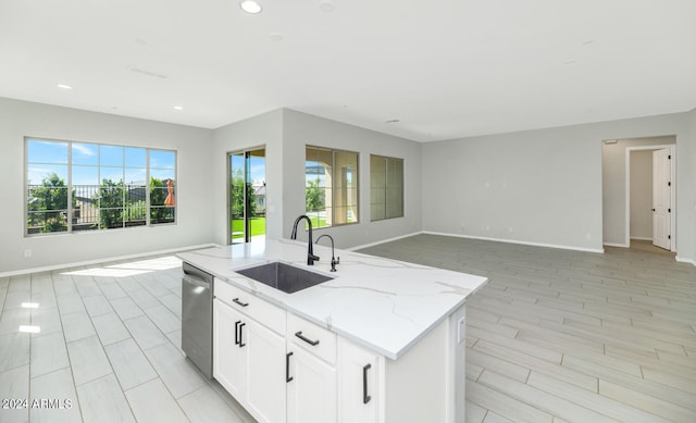 kitchen with dishwasher, a kitchen island with sink, sink, light stone counters, and white cabinetry